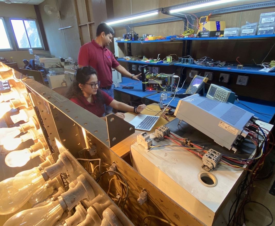 Two engineers running a load test with a long bank of lit incandescent lamps in the foreground