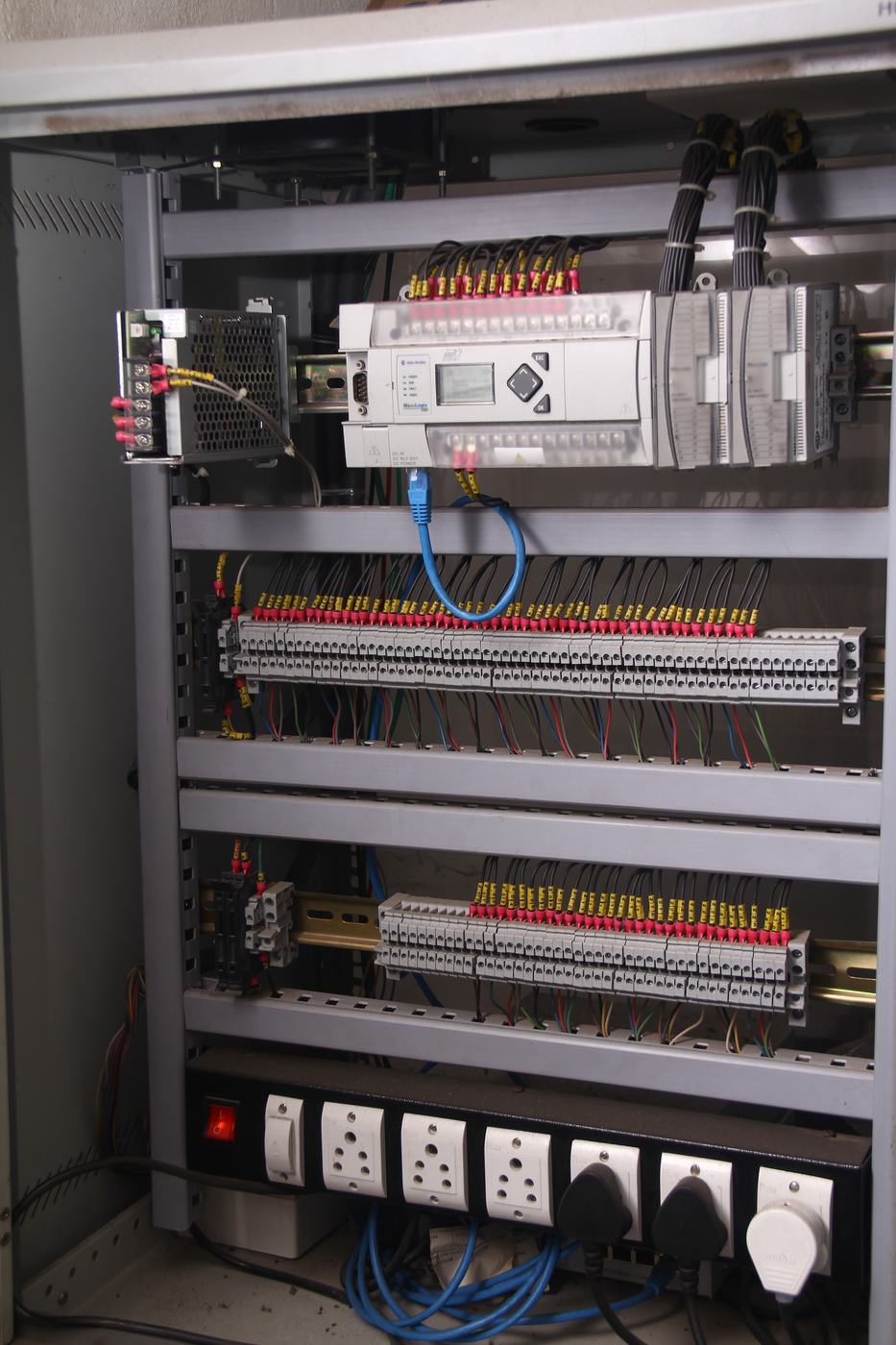 Wall-mounted panel with PLC, terminal rows and power sockets inside a relay hut